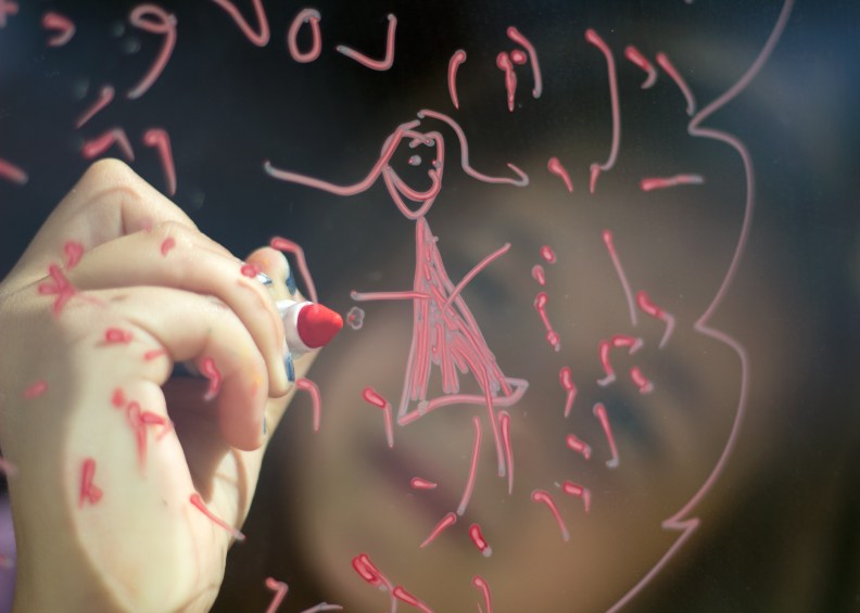 Girl drawing art on glass door with marker
